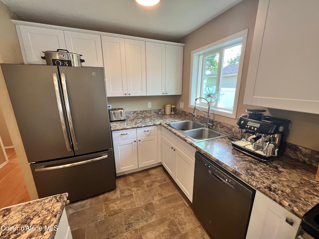 kitchen with a sink, stone finish flooring, white cabinetry, freestanding refrigerator, and dishwasher