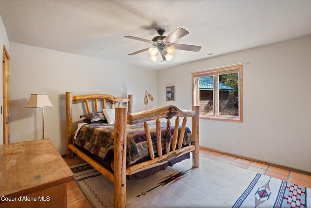 bedroom featuring ceiling fan, light tile patterned floors, and a textured ceiling