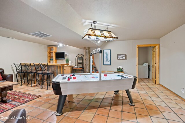 playroom with a textured ceiling, vaulted ceiling, light tile patterned floors, indoor bar, and washer / clothes dryer