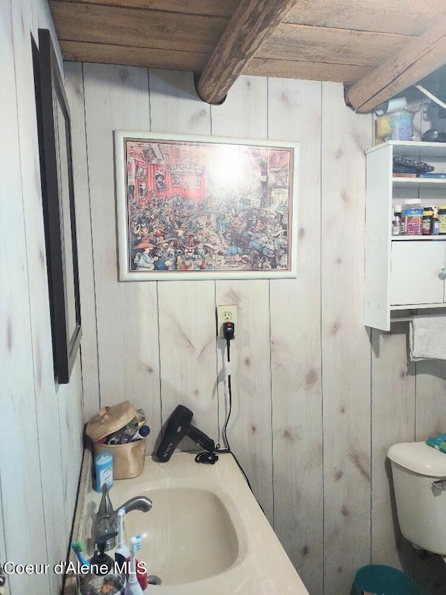 bathroom featuring beam ceiling, wood walls, toilet, and sink