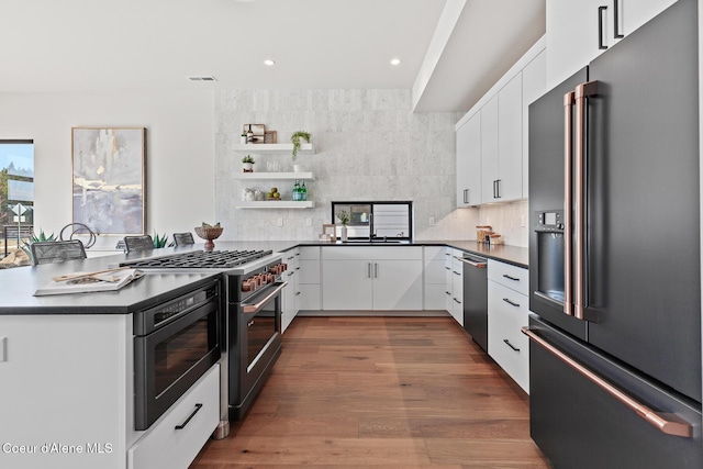 kitchen featuring dishwasher, high end fridge, gas range oven, and dark countertops