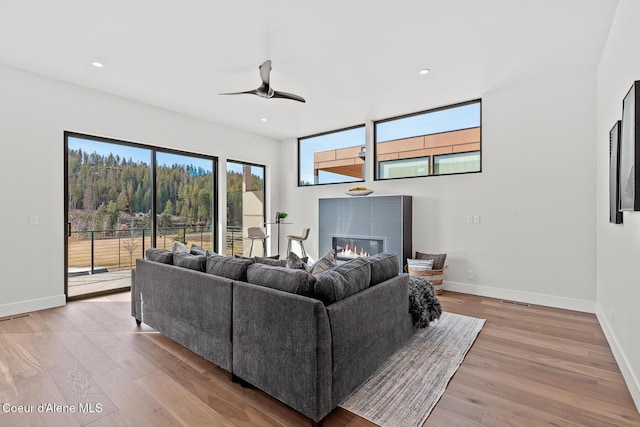 living room with light wood-style floors, baseboards, a ceiling fan, and a glass covered fireplace