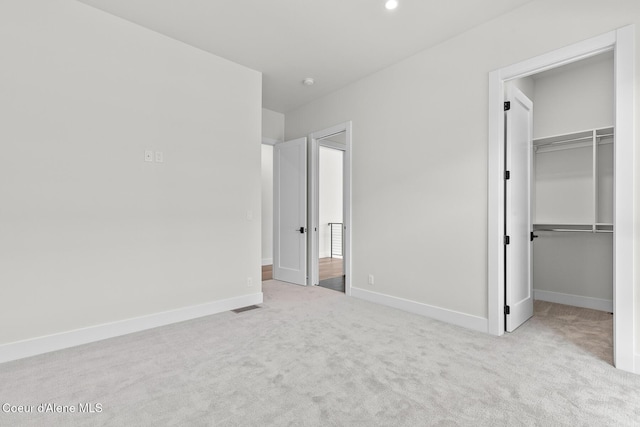 unfurnished bedroom with a walk in closet, carpet flooring, visible vents, and baseboards