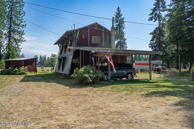 exterior space featuring a carport, a front yard, a chimney, and an outbuilding