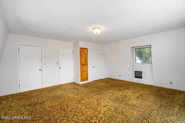 unfurnished bedroom with heating unit, a textured ceiling, two closets, and carpet