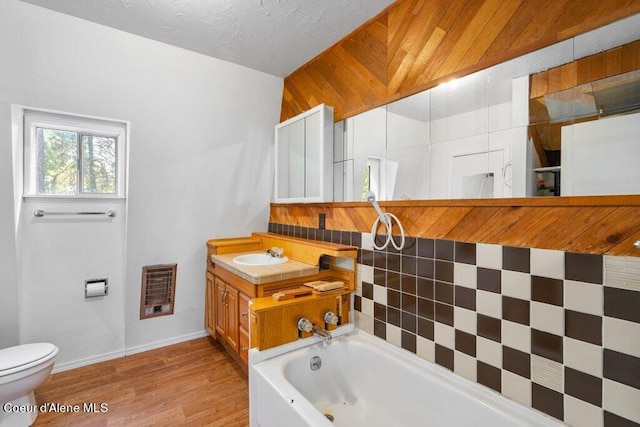full bath featuring a tub to relax in, heating unit, toilet, wood finished floors, and vanity