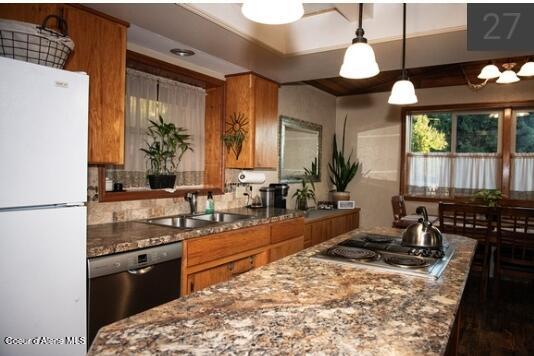 kitchen with light stone countertops, sink, stainless steel appliances, and decorative light fixtures