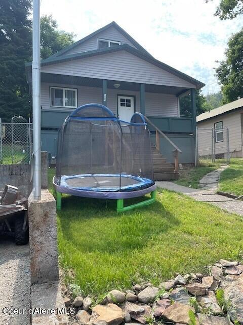 rear view of house featuring a trampoline and a lawn