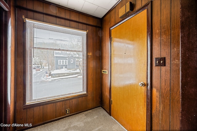 doorway to outside featuring light carpet and wooden walls