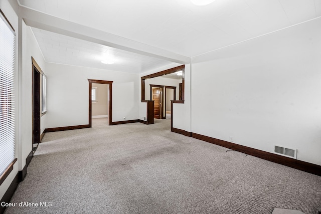 unfurnished room featuring beam ceiling, light carpet, and a wealth of natural light