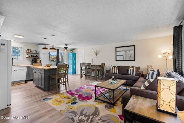 living room with ceiling fan, light wood-type flooring, and a textured ceiling