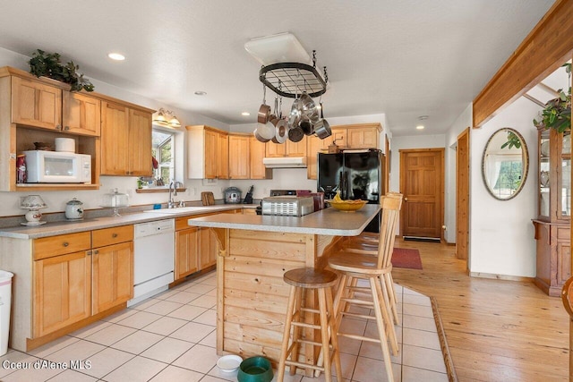 kitchen with a center island, light hardwood / wood-style floors, a kitchen bar, white appliances, and light brown cabinetry