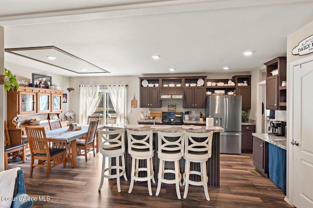 kitchen with a kitchen breakfast bar, light stone countertops, dark hardwood / wood-style floors, stainless steel refrigerator with ice dispenser, and a kitchen island