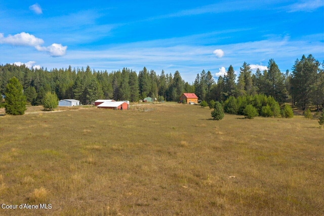 view of yard with a rural view, an outdoor structure, and a view of trees