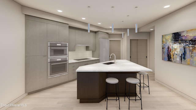 kitchen featuring a sink, double oven, light countertops, gray cabinets, and a kitchen island with sink