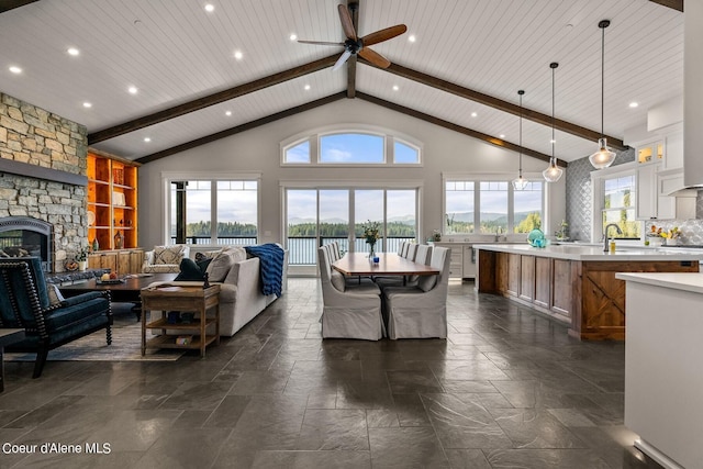 8491 N Mckinley Ln, Hayden, ID 83835 - living room with high vaulted ceiling, beamed ceiling, a ceiling fan, a stone fireplace, and stone tile floors