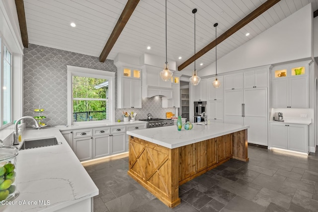 8491 N Mckinley Ln, Hayden, ID 83835 - kitchen featuring decorative backsplash, beamed ceiling, light stone countertops, a center island with sink, and a sink