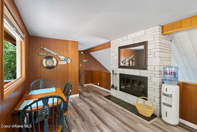 living area with wooden walls, a stone fireplace, and wood finished floors