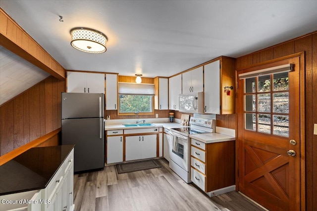 kitchen featuring light wood-style floors, white cabinetry, a sink, wooden walls, and white appliances