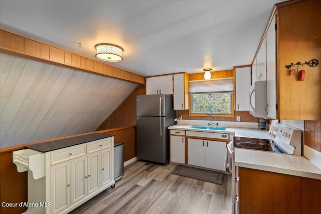 kitchen with white appliances, wood walls, a sink, vaulted ceiling, and light wood-type flooring