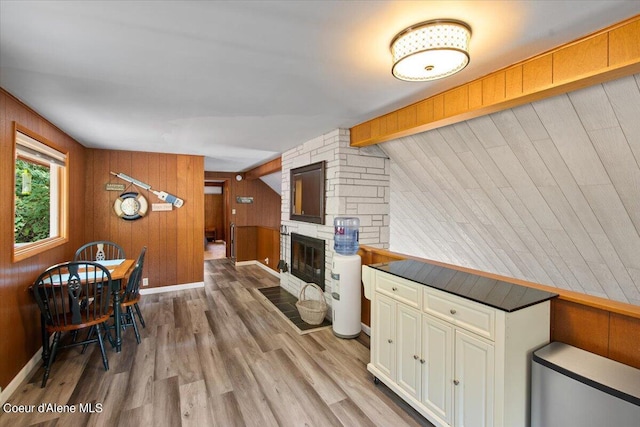 kitchen featuring vaulted ceiling with beams, white cabinets, a stone fireplace, wood finished floors, and baseboards