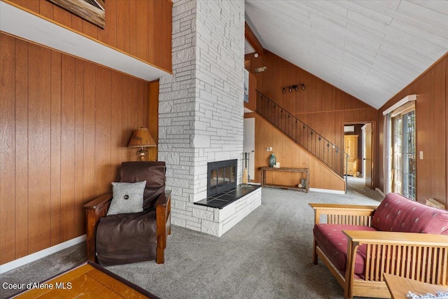 living room with carpet floors, a stone fireplace, stairway, and wooden walls