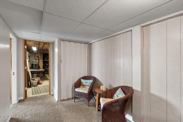 living area featuring carpet floors, a paneled ceiling, and wooden walls