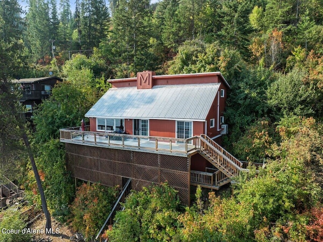 back of house featuring stairs, metal roof, a deck, and a view of trees