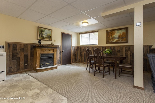 dining space with a paneled ceiling, wood walls, and light colored carpet