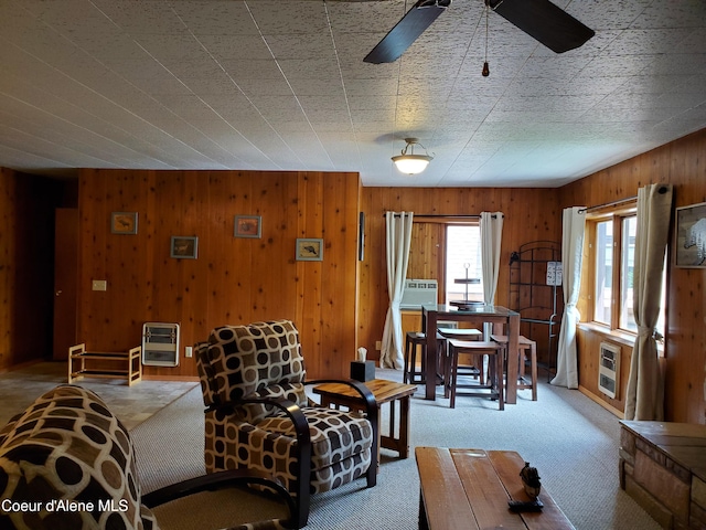 carpeted living room with ceiling fan, wooden walls, and heating unit