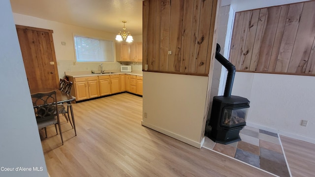 kitchen featuring a wood stove, sink, hanging light fixtures, a notable chandelier, and light hardwood / wood-style floors