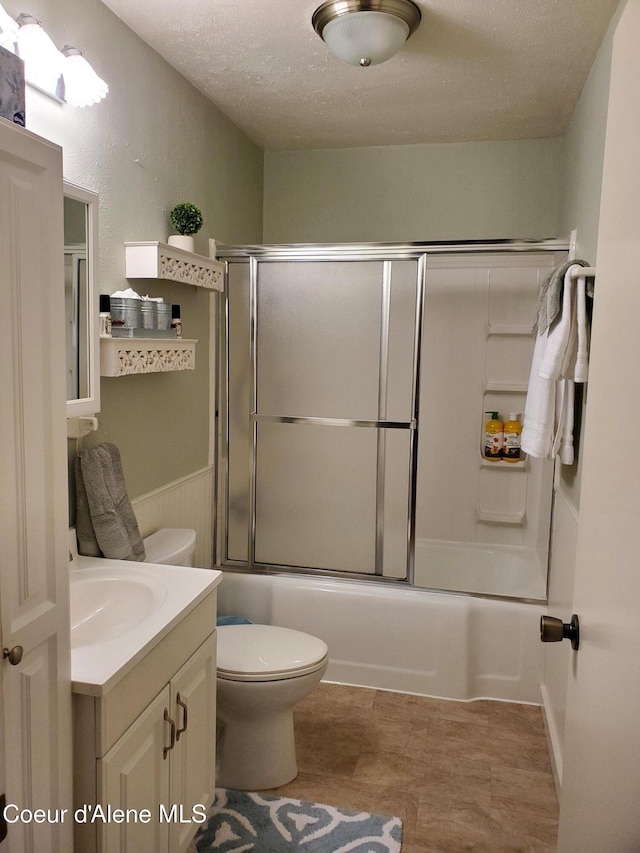 full bathroom featuring combined bath / shower with glass door, vanity, a textured ceiling, and toilet