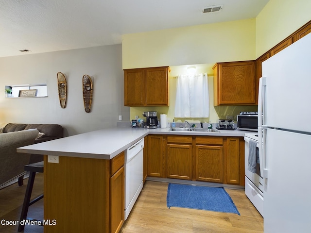 kitchen with sink, light hardwood / wood-style flooring, kitchen peninsula, white appliances, and a kitchen bar