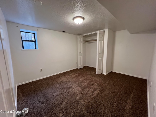 unfurnished bedroom with dark colored carpet, a textured ceiling, and a closet