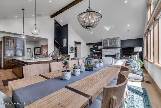 dining area with beamed ceiling, light wood-type flooring, sink, high vaulted ceiling, and a fireplace