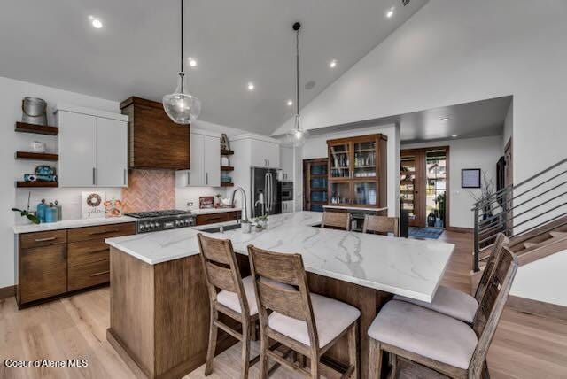 kitchen featuring pendant lighting, white cabinets, high vaulted ceiling, and a kitchen island with sink