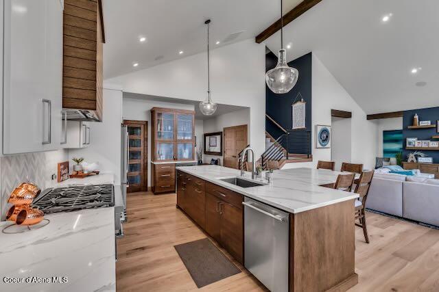 kitchen featuring appliances with stainless steel finishes, light hardwood / wood-style floors, sink, and high vaulted ceiling