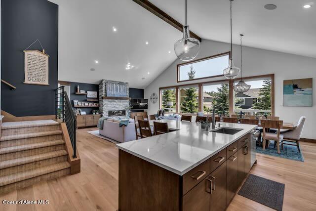 kitchen featuring dark brown cabinets, sink, light hardwood / wood-style flooring, a center island with sink, and a stone fireplace