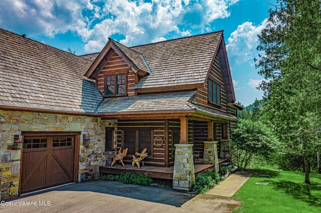 log cabin featuring a front yard, an attached garage, stone siding, and a porch