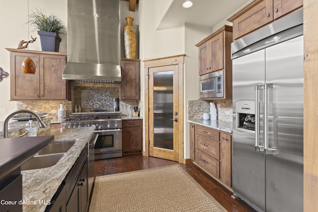 kitchen featuring dark wood finished floors, backsplash, a sink, built in appliances, and wall chimney range hood