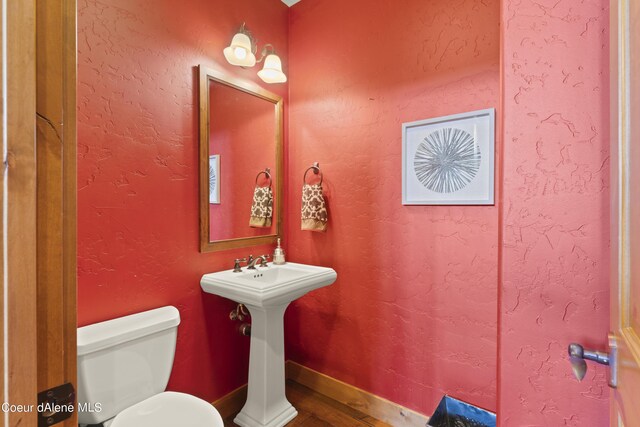 bathroom featuring toilet, a textured wall, and baseboards