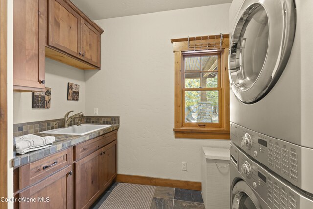 laundry area with stone finish floor, baseboards, a sink, stacked washer and dryer, and cabinet space
