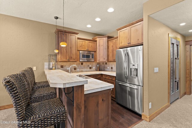 kitchen featuring light countertops, a sink, backsplash, appliances with stainless steel finishes, and a peninsula