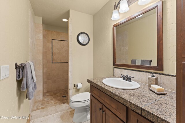 full bathroom with a textured wall, a tile shower, toilet, and vanity