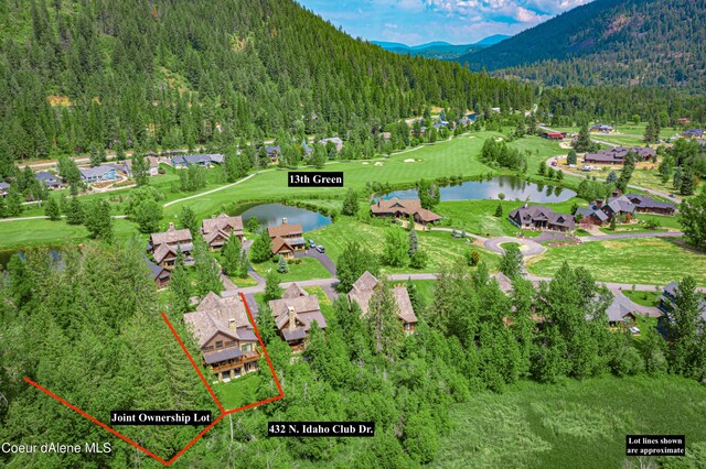 drone / aerial view with view of golf course, a view of trees, and a water and mountain view