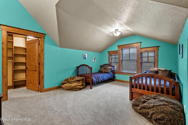 bedroom with vaulted ceiling, carpet floors, a spacious closet, a textured ceiling, and baseboards