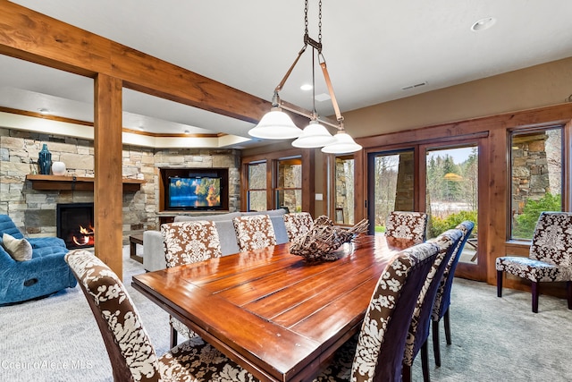 carpeted dining room with a fireplace, visible vents, beamed ceiling, and a wealth of natural light