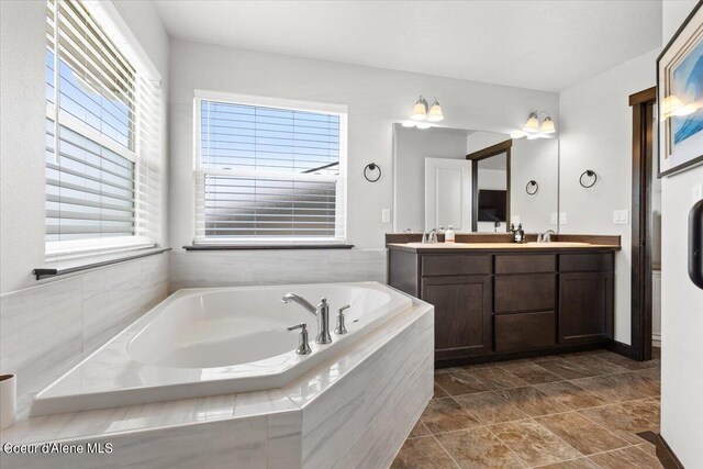 bathroom featuring vanity, a relaxing tiled tub, and a healthy amount of sunlight