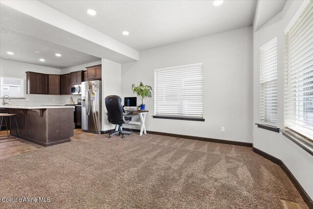 kitchen with a wealth of natural light, stainless steel appliances, light colored carpet, and a breakfast bar