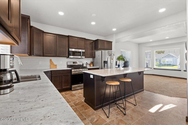 kitchen featuring a kitchen island, a breakfast bar area, light stone countertops, appliances with stainless steel finishes, and sink